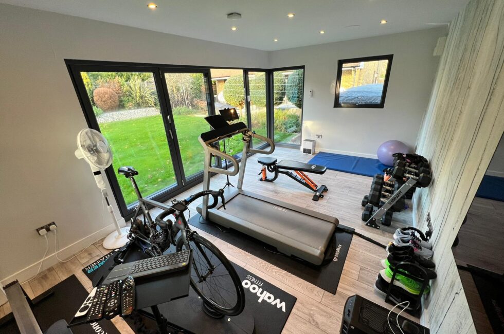 A hi tech garden room with gym equipment including a stationary bike, treadmill, weights, and yoga mat