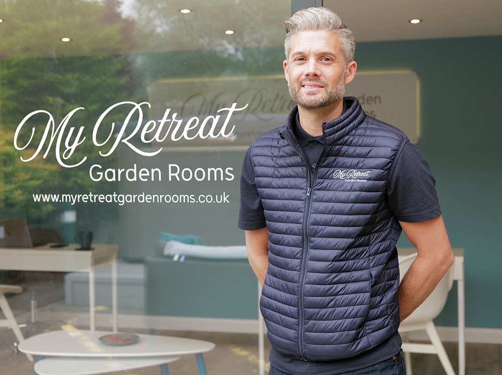 Kieron Summerhayes, founder of My Retreat Garden Rooms, in front of the company logo