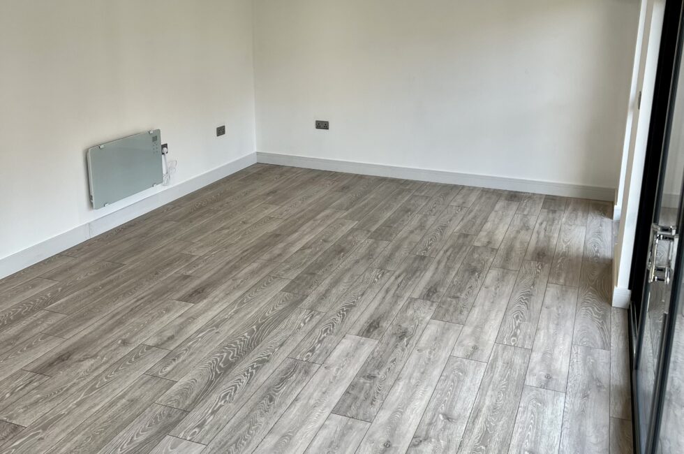 Inside of a 7m x 4m garden room with laminate grey floor and large sliding doors