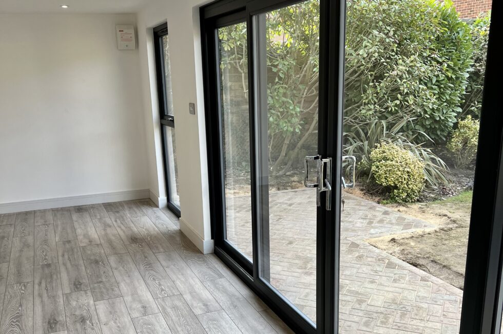Inside of a 7m x 4m garden room with laminate grey floor and large sliding doors