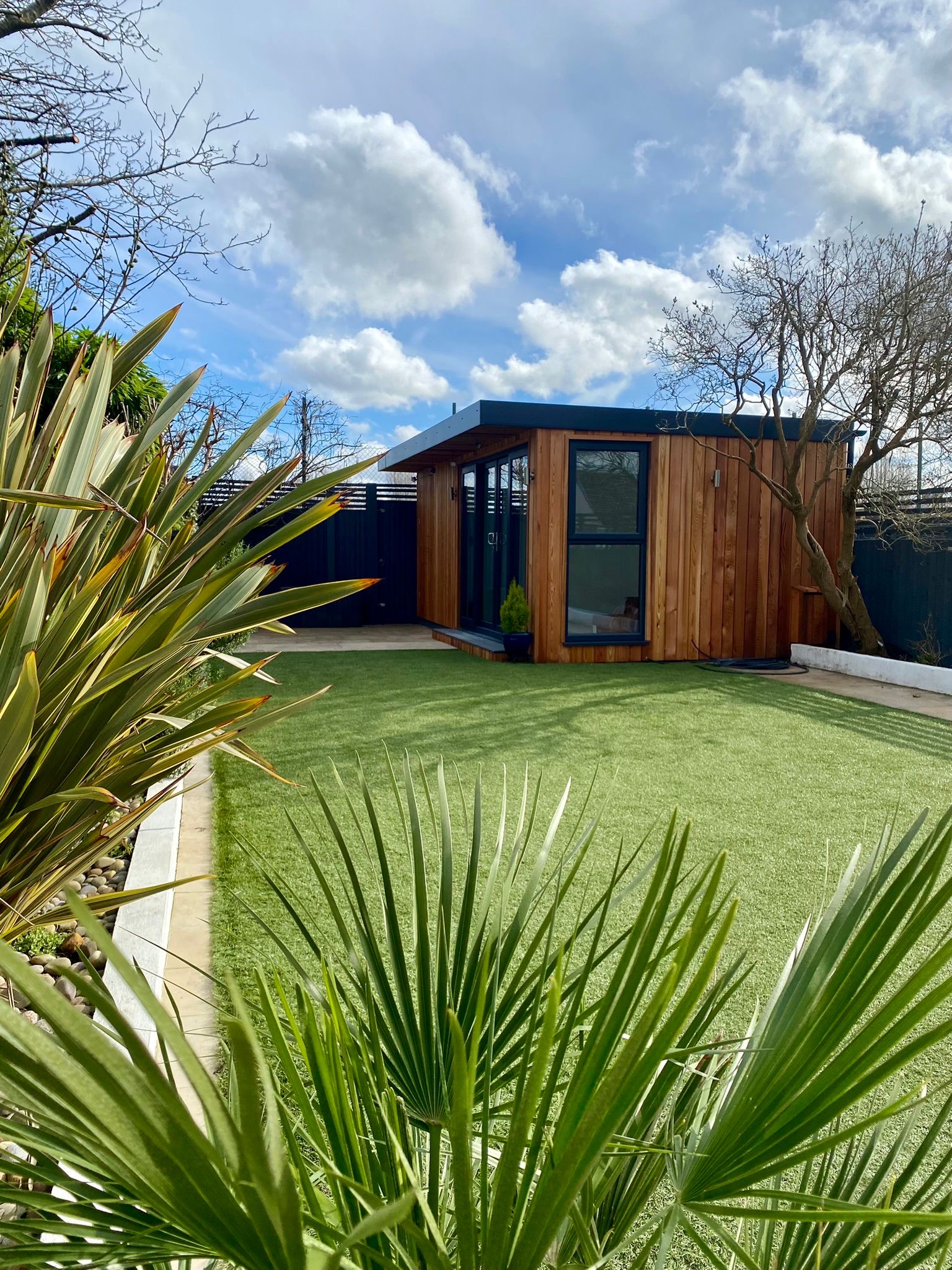 Cedar-clad My Retreat garden room with uPVC anthracite grey sliding doors set in a Surrey garden with artificial grass
