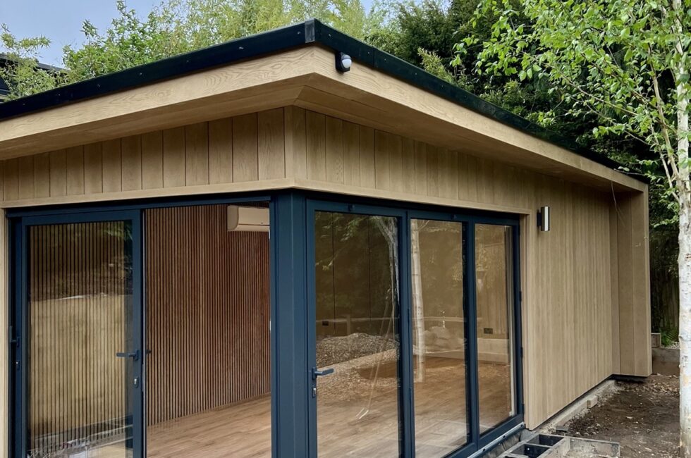 This 7.5 x 4m garden room features Millboard Envelop Shadow Cline Golden Oak Cladding, offering minimal maintenance and a striking colour against the anthracite grey aluminium sliding and bifold doors.