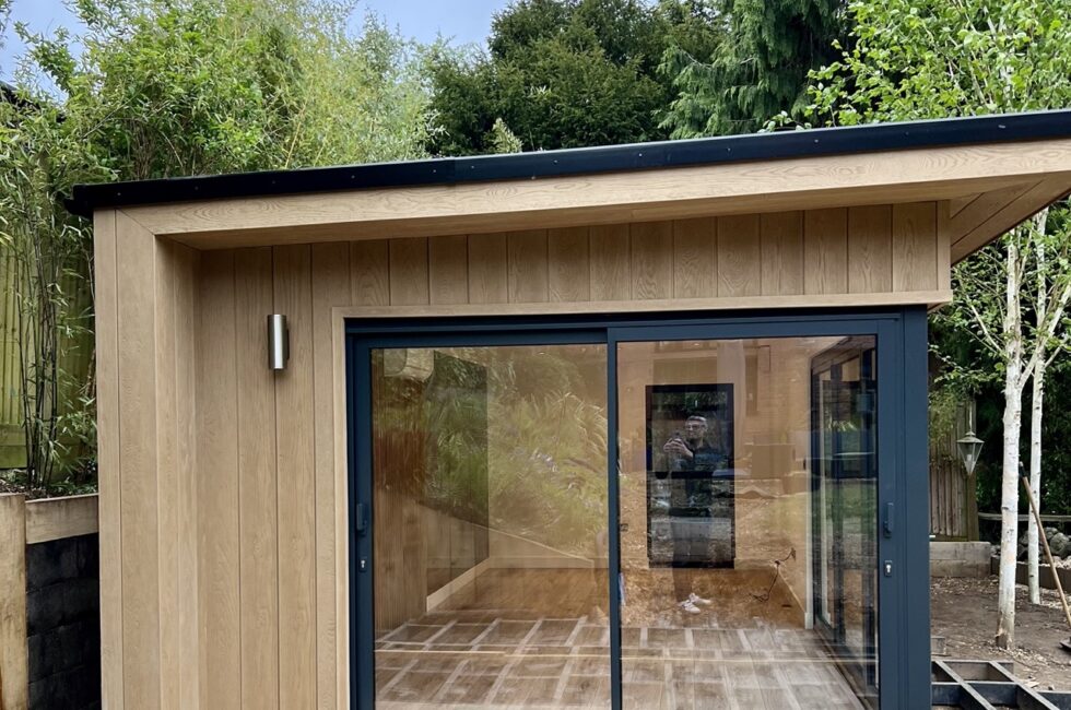 This 7.5 x 4m garden room features Millboard Envelop Shadow Cline Golden Oak Cladding, offering minimal maintenance and a striking colour against the anthracite grey aluminium sliding and bifold doors.