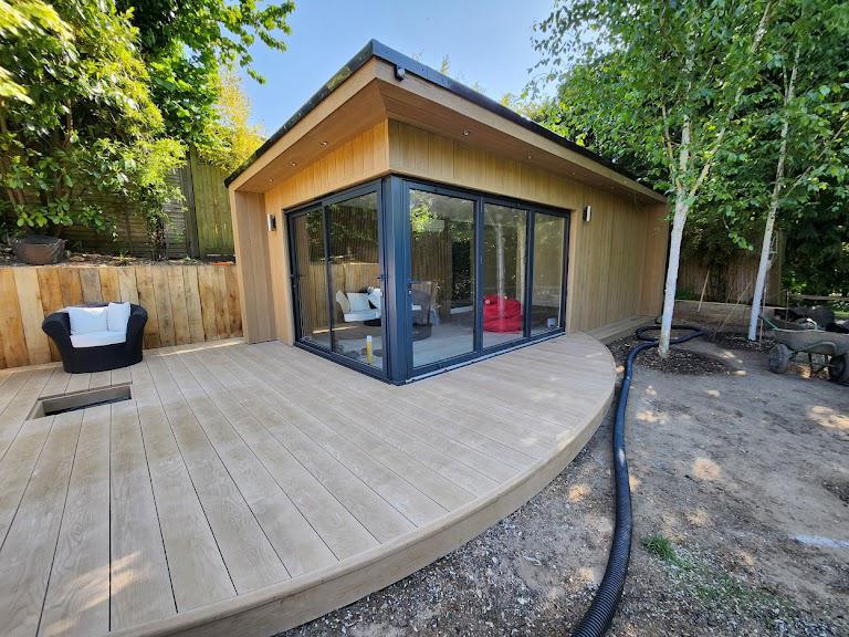 Golden oak Millboard composite garden room with bifold doors creating a glass corner and circular patio entertaining area