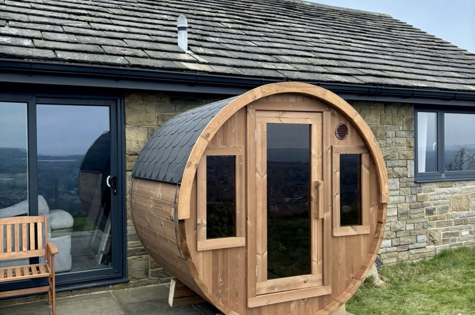 Barrel sauna made from Thermowood, featuring bronze-tinted glass windows and doors, set in a garden.