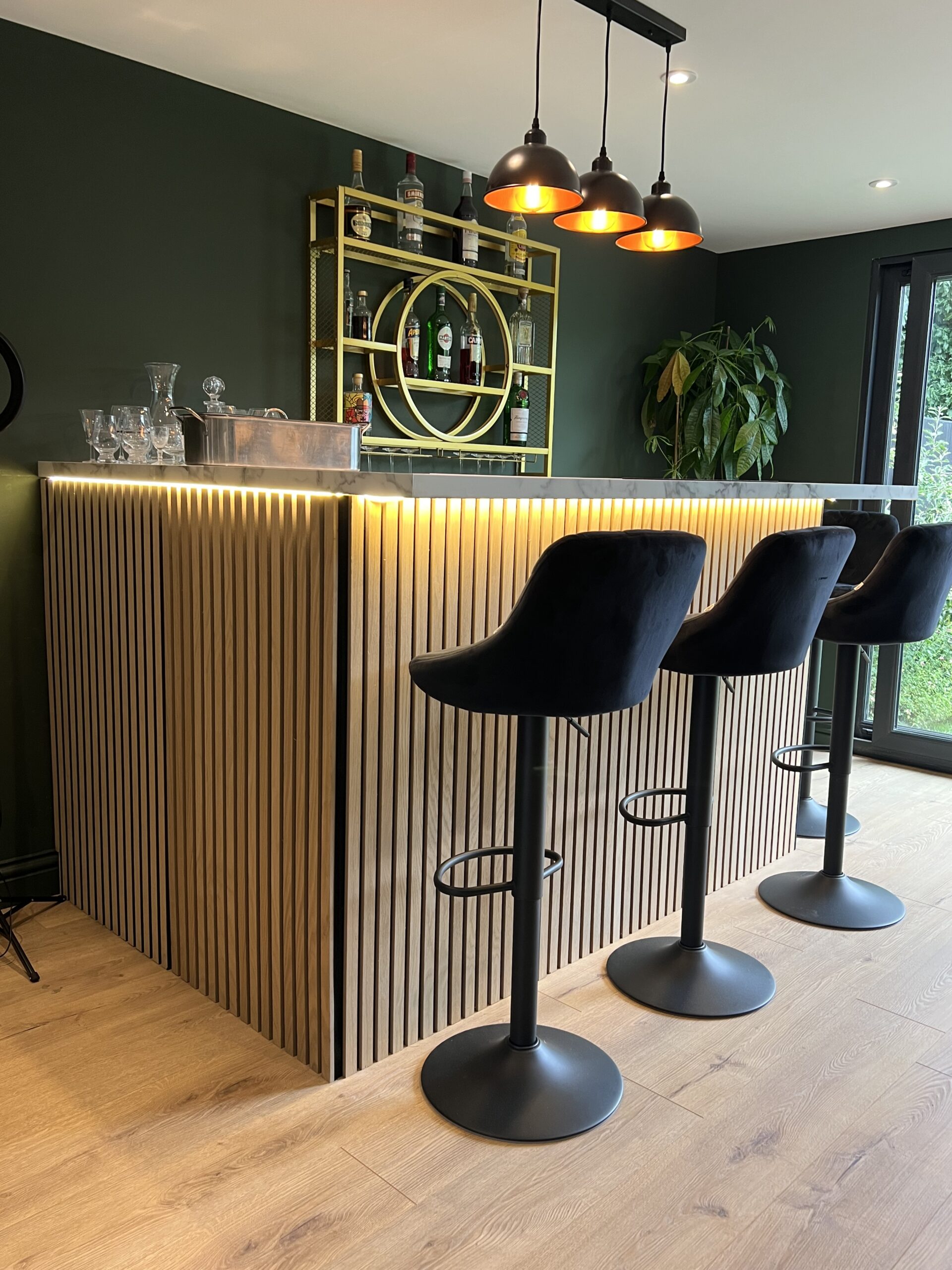 Bespoke garden bar room built by My Retreat Garden Rooms in Surrey, black composite cladding with sliding doors and warm interior lighting at dusk