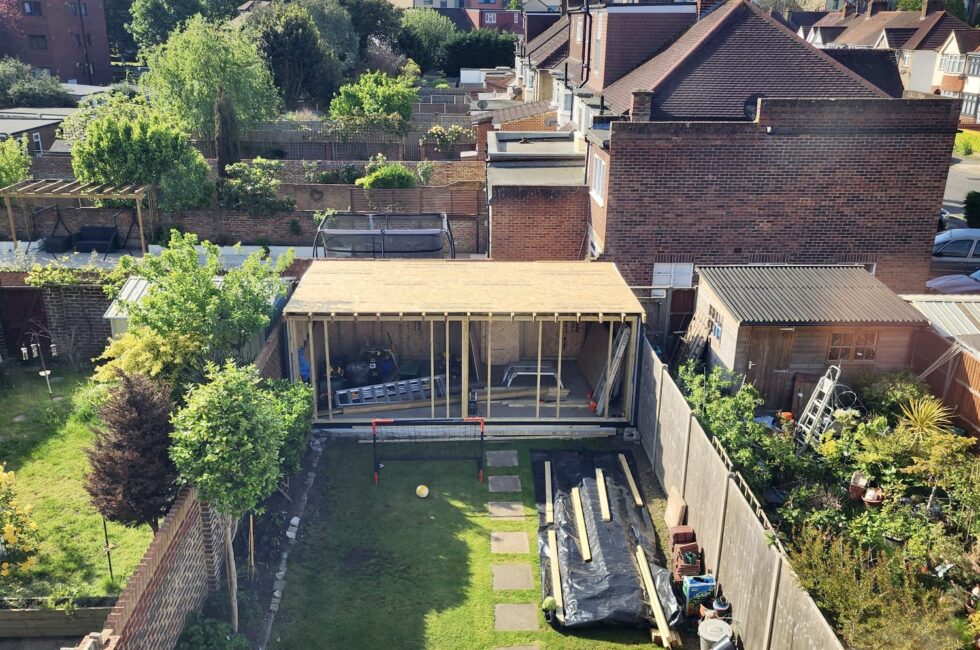 Timber frame garden room under construction in a residential garden before cladding and insulation installation