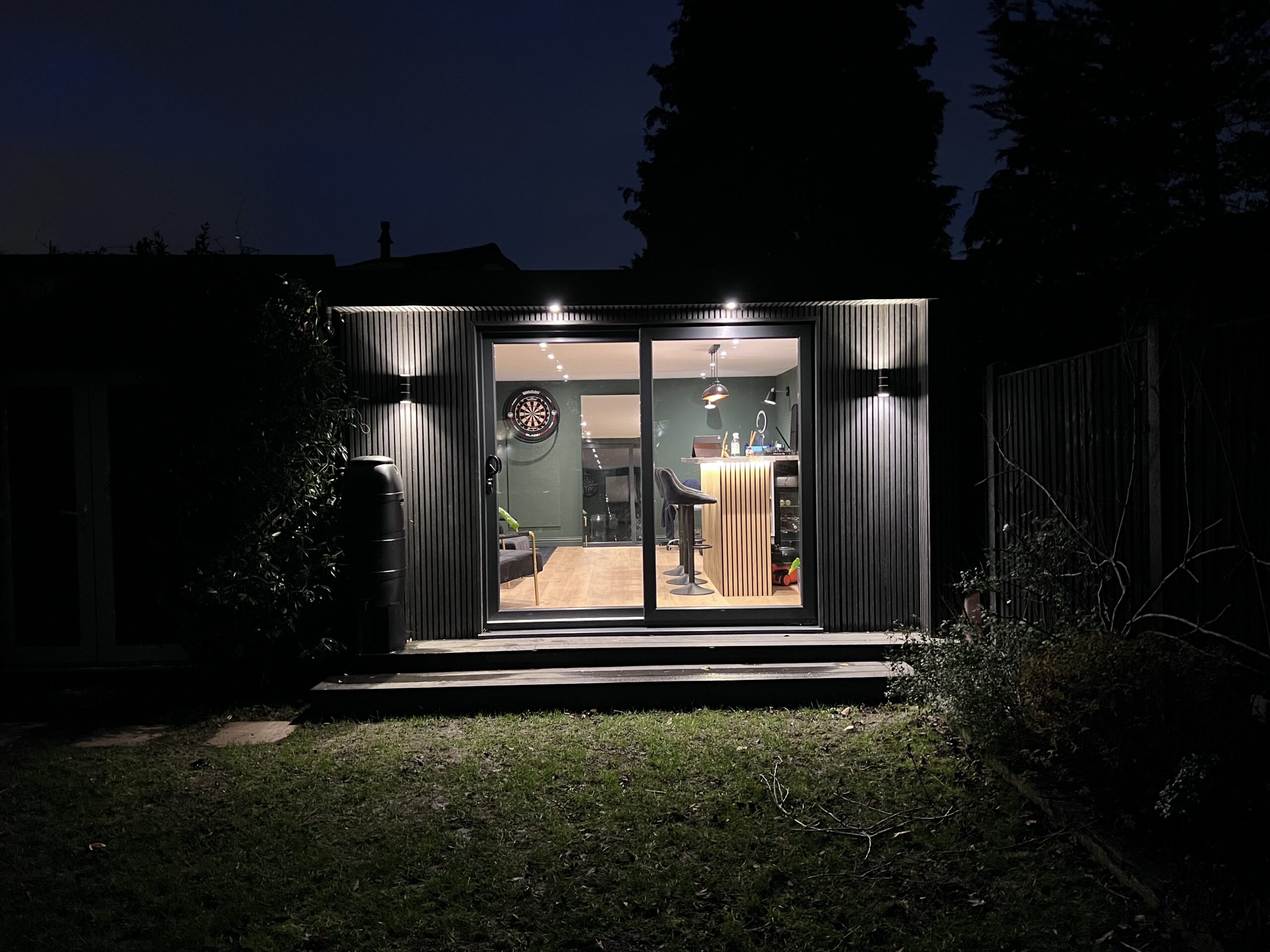 Garden bar room at night lit up from inside, dart board and bar visible through sliding doors, Surrey