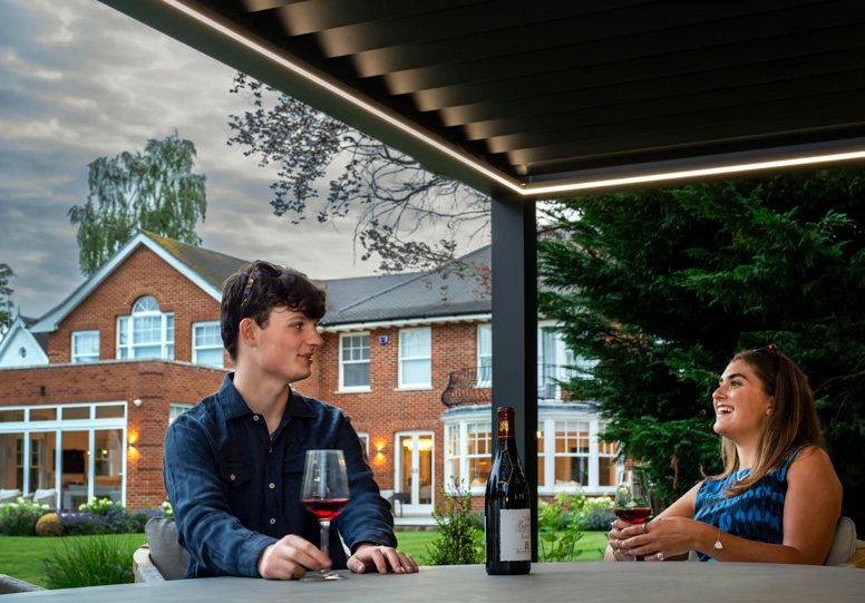 Couple relaxing under a louvred pergola with integrated LED lighting in the evening