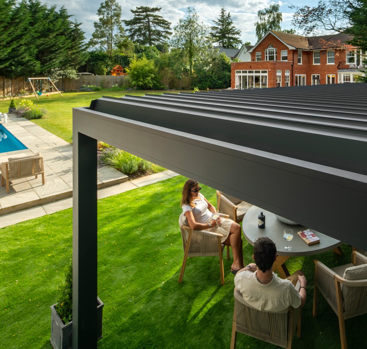 Louvred aluminium pergola over garden seating on a lawn with a house behind